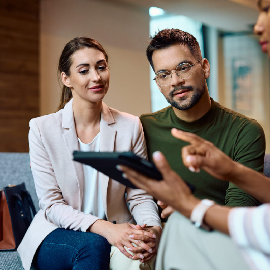 Young couple listening their financial advisor who is using touchpad during a meeting in the office.